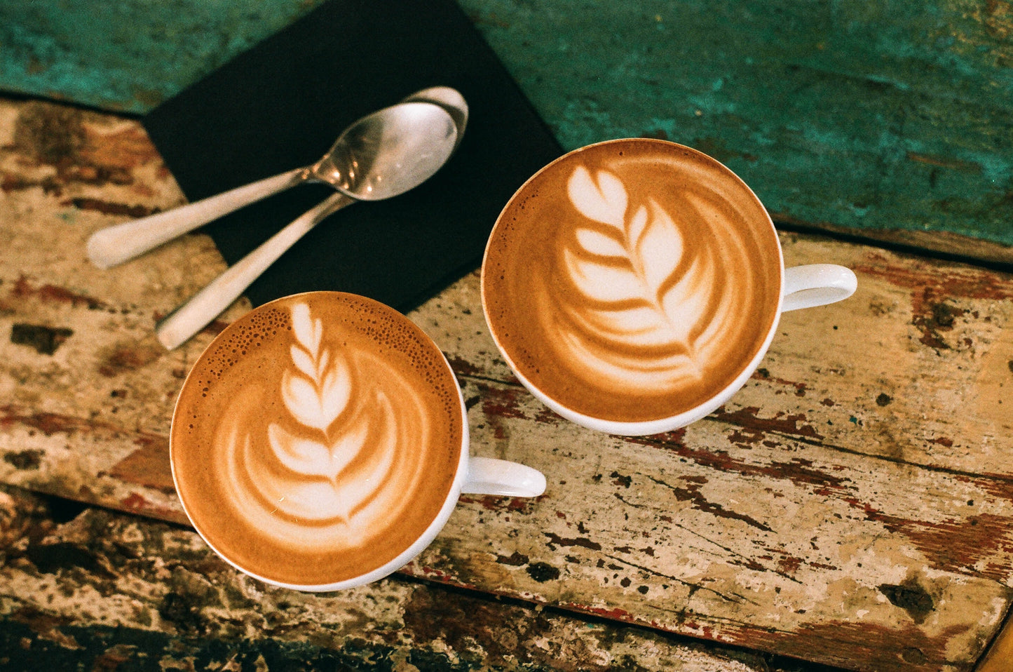 two coffee cups with latte art and two spoons on rustic wood