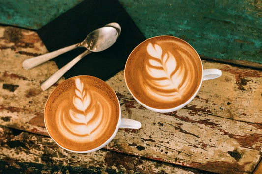 two coffee cups with latte art and two spoons on rustic wood